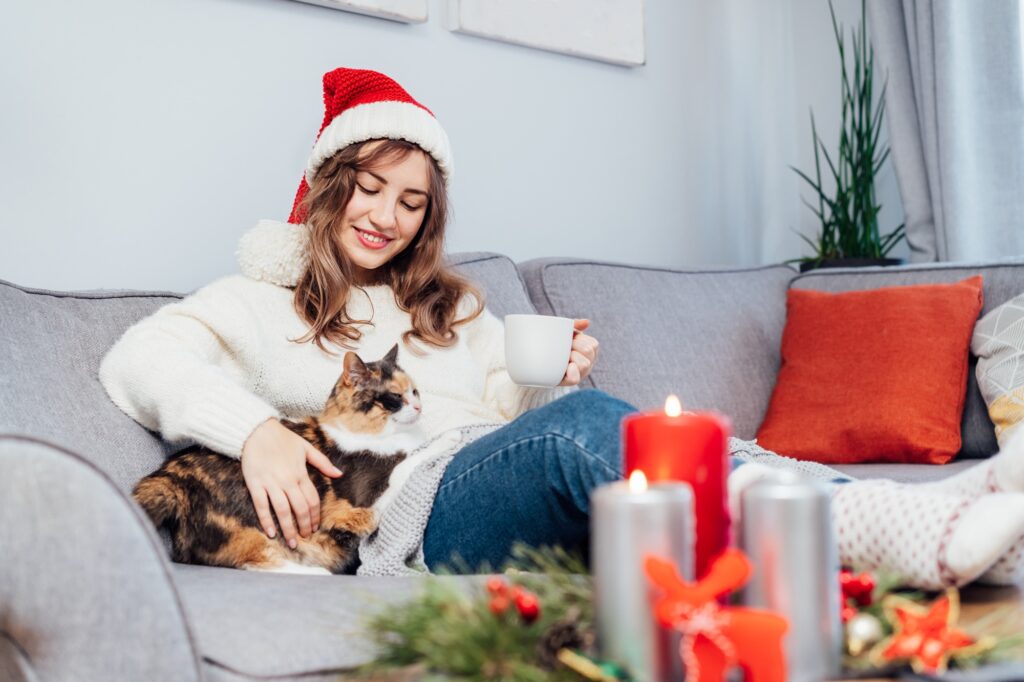Woman in plaid with tea cup watching movie, TV with cat pet on sofa at home with christmas mood